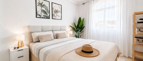 Un dormitorio ordenado con cama, mesita de noche, lámpara y un sombrero sobre la cama.