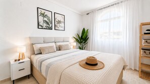 A neatly arranged bedroom with a bed, bedside table, lamp, and a hat on the bed.