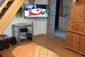 En stue med et fjernsyn monteret på væggen, et lille bord med højttalere, et træskab og en trappe.