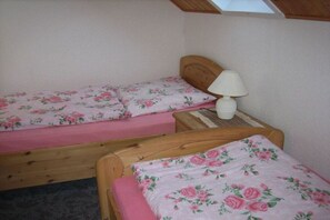 A bedroom with two single beds, each with a floral bedspread and a wooden headboard. There is a bedside table with a lamp and a small table between the beds. - Holiday home with 1 bedroom (Breitenbrunn OT Rittersgrün)