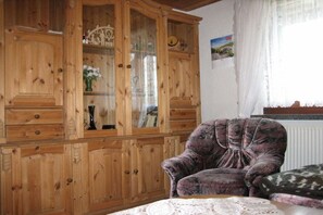 A wooden cabinet with glass doors, a cushioned armchair, and a table with a lace tablecloth. - Holiday home with 1 bedroom (Breitenbrunn OT Rittersgrün)