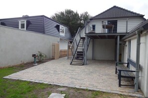 Ein Wohnhaus mit Pflasterterrasse, einer Treppe zu einem zweiten Stockwerk und einer Bank.
