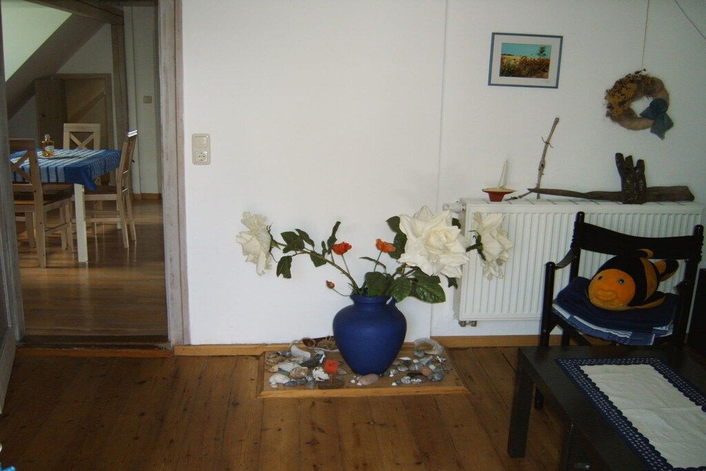 A room with a blue vase on a wooden base, a white radiator, and a chair with a cushion.