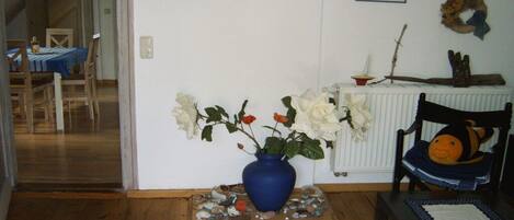 Una habitación con un jarrón azul sobre una base de madera, un radiador blanco y una silla con cojín.