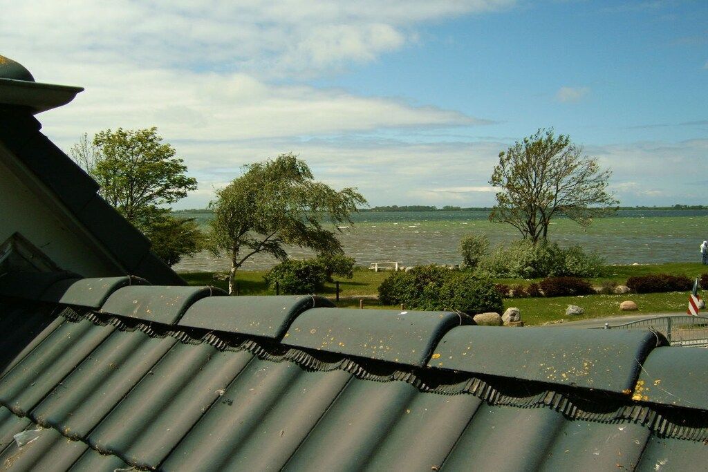 A view of a roof with a metal gutter and a body of water in the background.