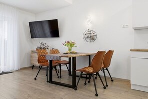 A modern dining area with a wooden table, leather chairs, a flat-screen TV mounted on the wall, and a decorative wall piece. - Holiday apartment in Zinnowitz with Wi-Fi (Zinnowitz)