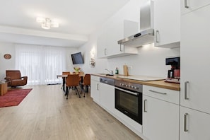 A modern kitchen with white cabinetry, a built-in oven, and a dining area with a table and chairs. - Holiday apartment in Zinnowitz with Wi-Fi (Zinnowitz)