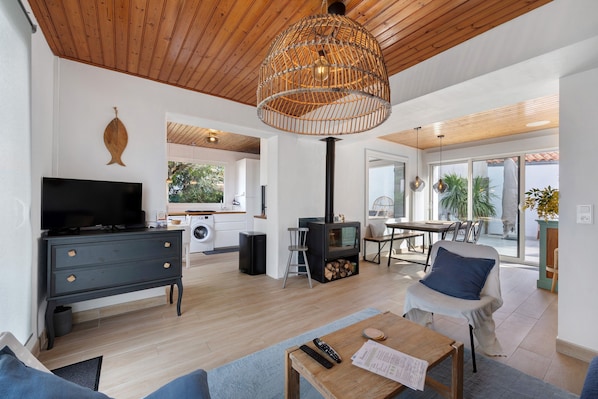A modern living room with a television, sofa, coffee table, and a large wicker chandelier.