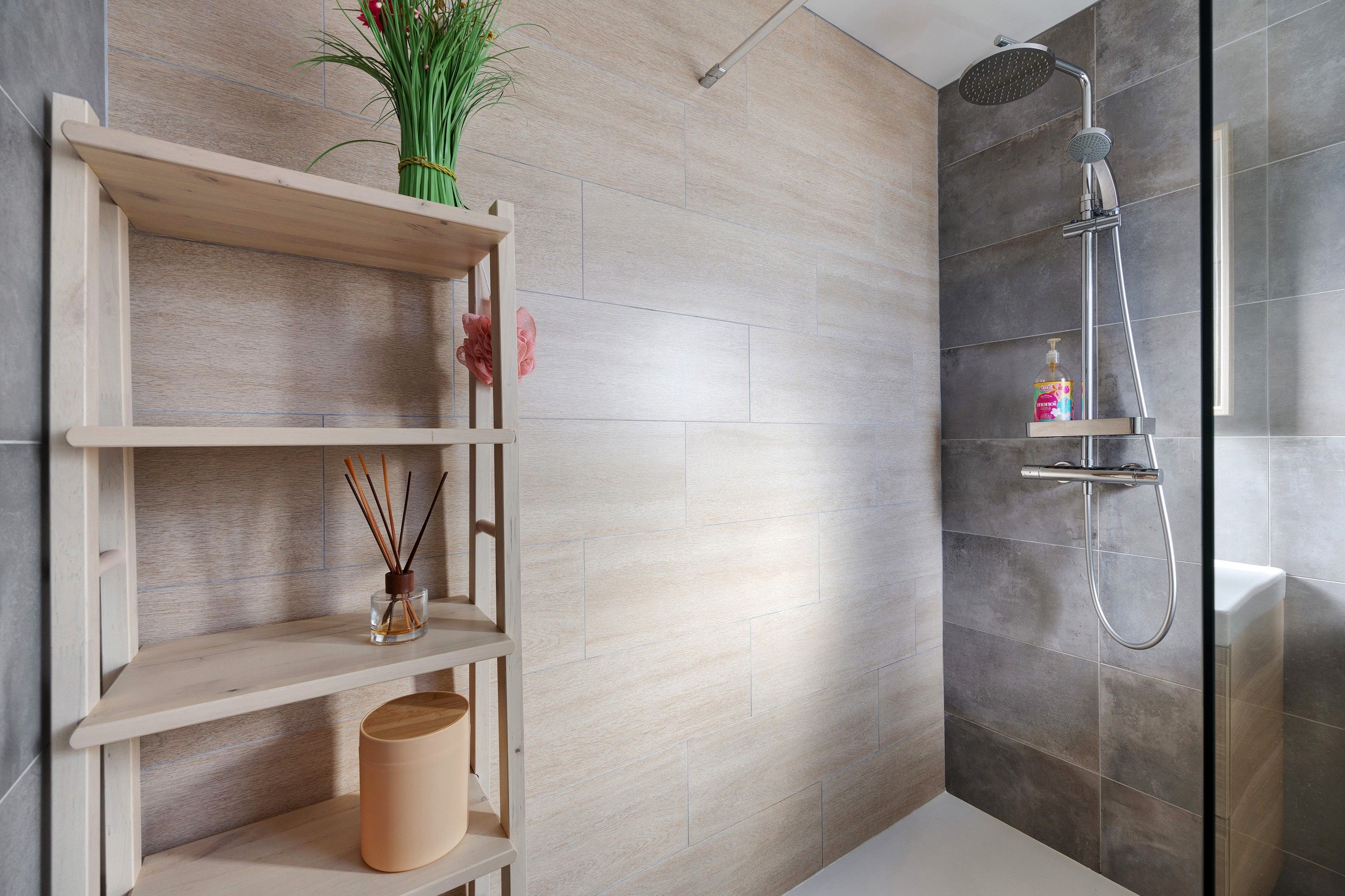 Een moderne badkamer met een douche, een houten plankje met decoratieve spullen en een toilet.