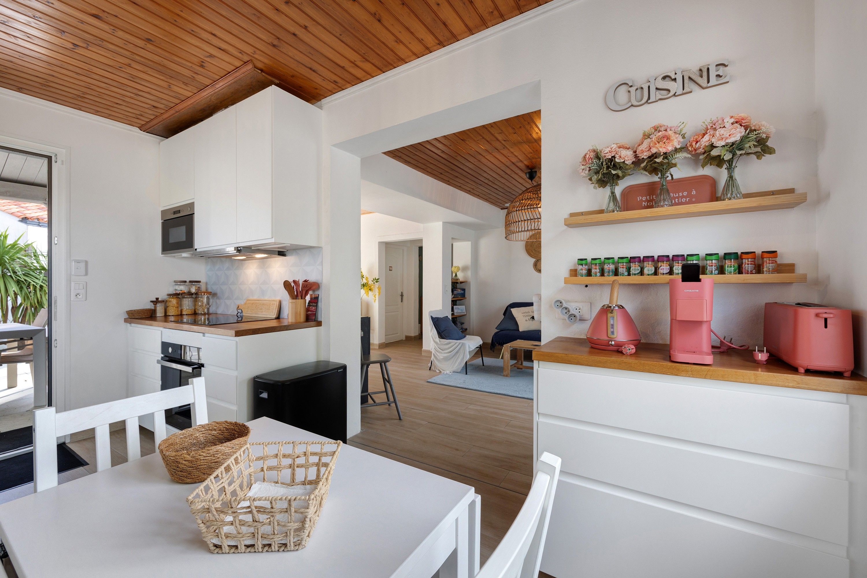 Una cocina moderna con armarios blancos, techo de madera y encimera con electrodomésticos.
