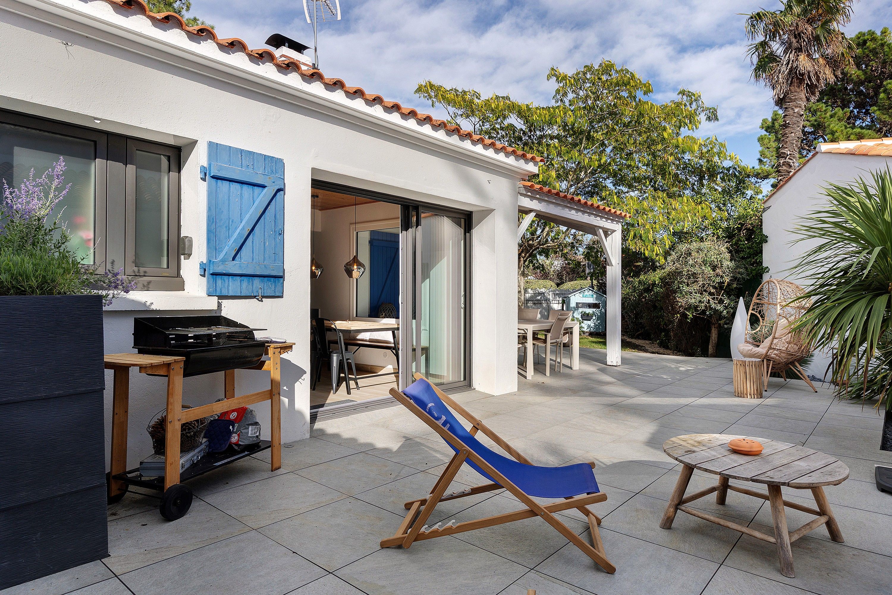 Un patio con una parrilla, una silla reclinable azul y una mesita con un cuenco.