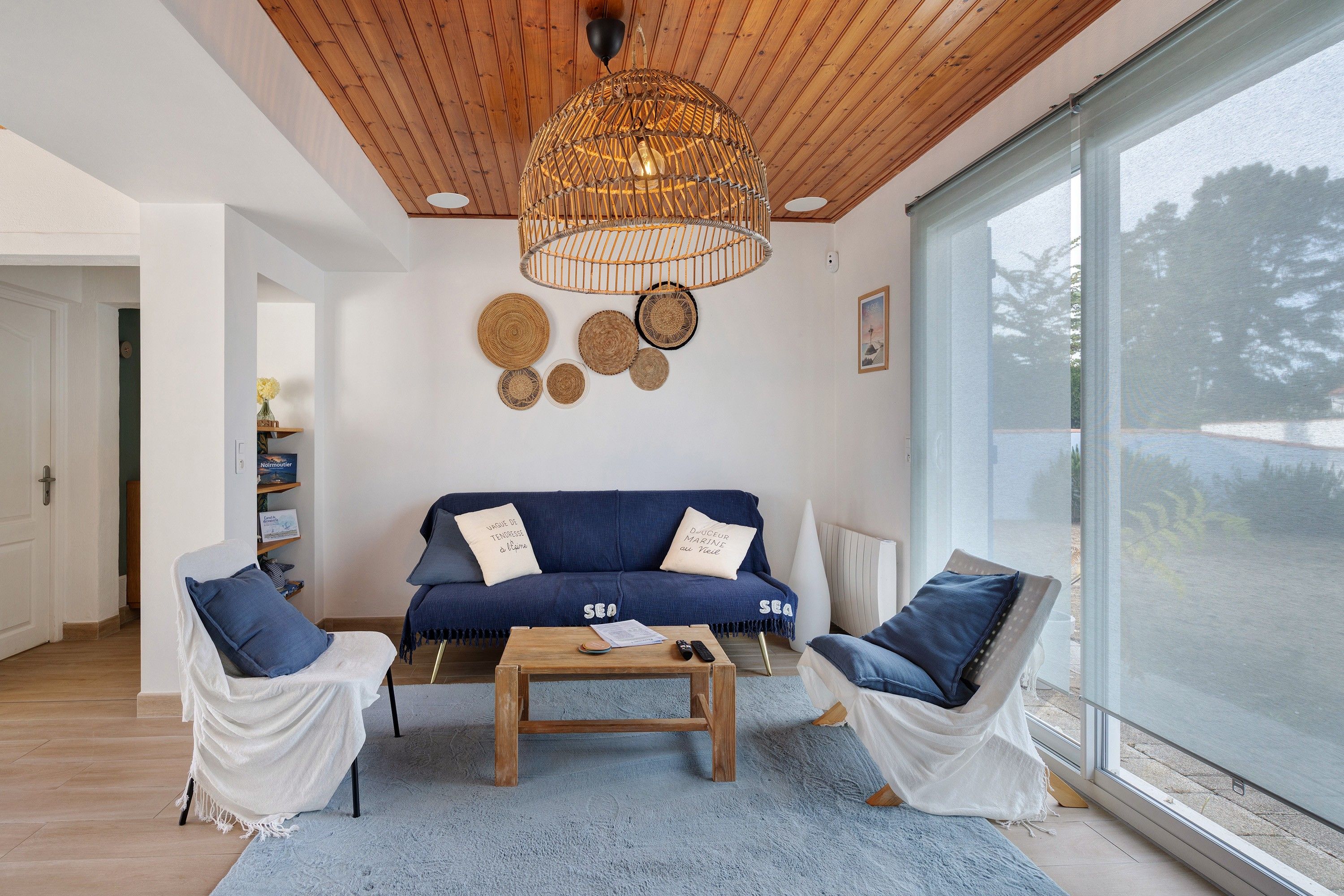 Een moderne woonkamer met een blauwe bank, twee fauteuils, een houten salontafel en een groot raam.