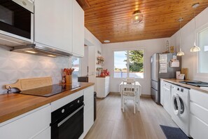 Una cuina moderna amb terra de fusta, armaris blancs, forn de sobretaula, rentadora i zona de menjador amb taula i cadires.