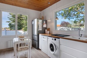 Cocina compacta con lavadora, refrigerador y comedor con mesa y sillas.