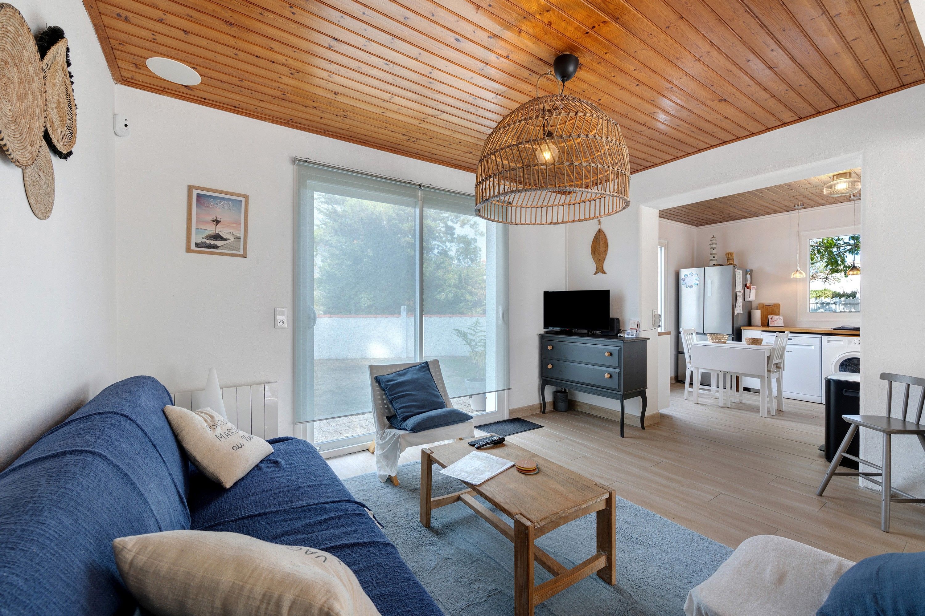 A modern living room with a sofa, coffee table, and a TV. There's a kitchen area with a fridge, stove, and sink.