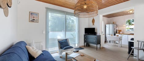 A modern living room with a sofa, coffee table, and a TV. There's a kitchen area with a fridge, stove, and sink.