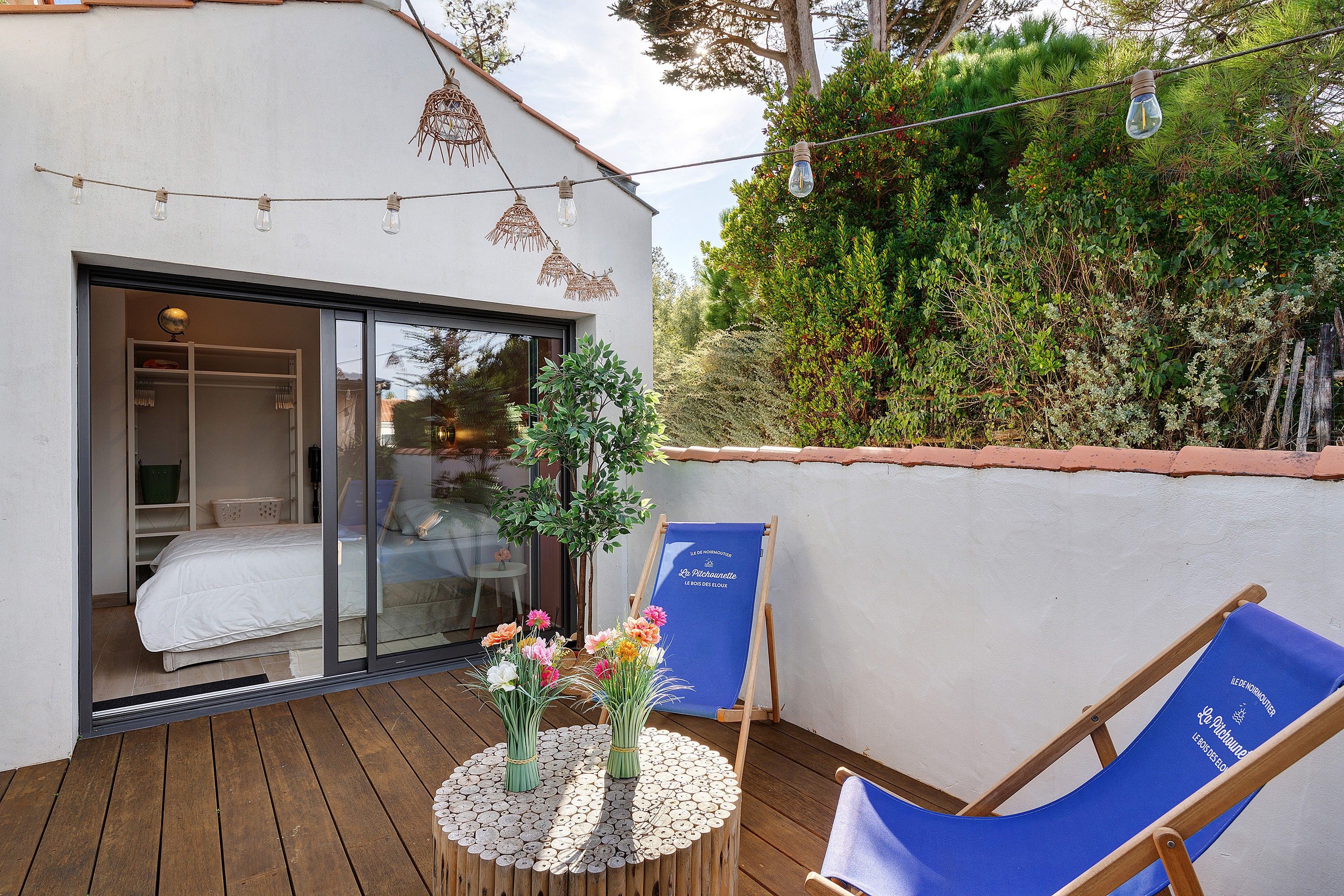 Una terraza de madera con una mesa, sillas y un ventanal que da a una habitación.