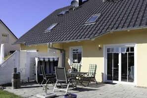 Ein Haus mit Ziegeldach, einer überdachten Terrasse mit Stühlen und Tisch sowie einer Glasschiebetür.