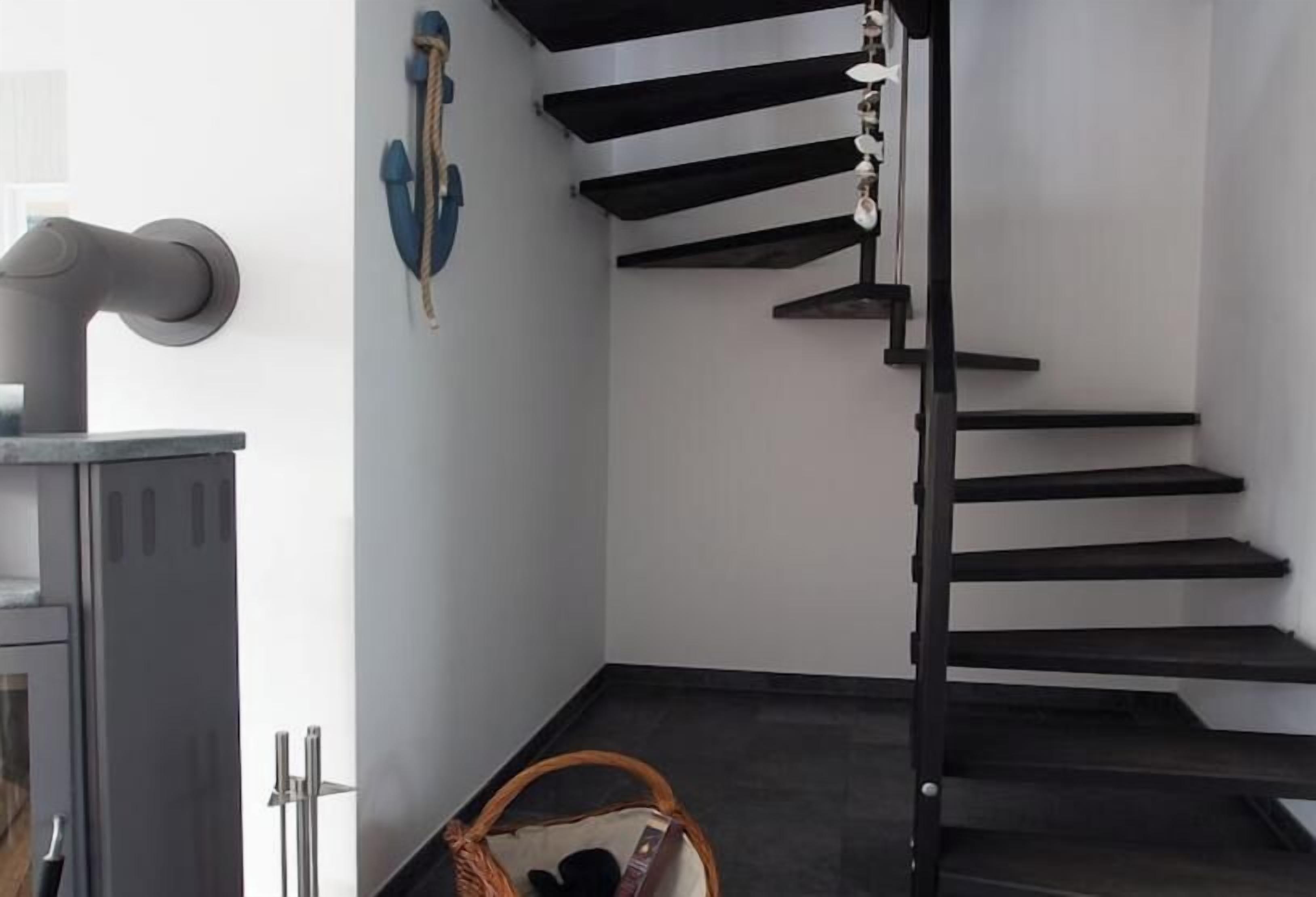 Una escalera de diseño moderno, un perchero de pared y una cesta en el suelo.