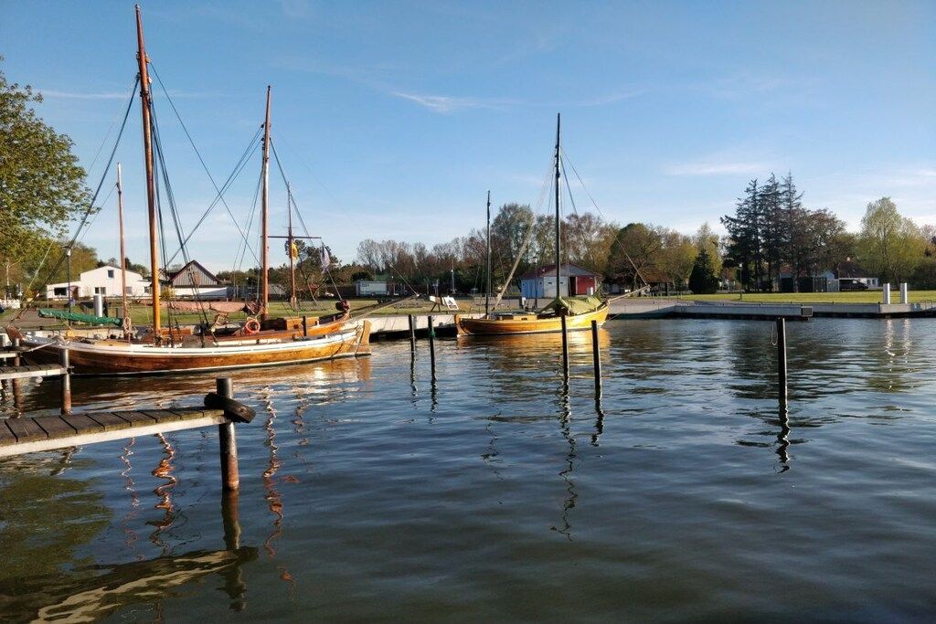 Un plan d’eau calme où sont amarrés des bateaux, avec un quai et un petit bâtiment en arrière-plan.