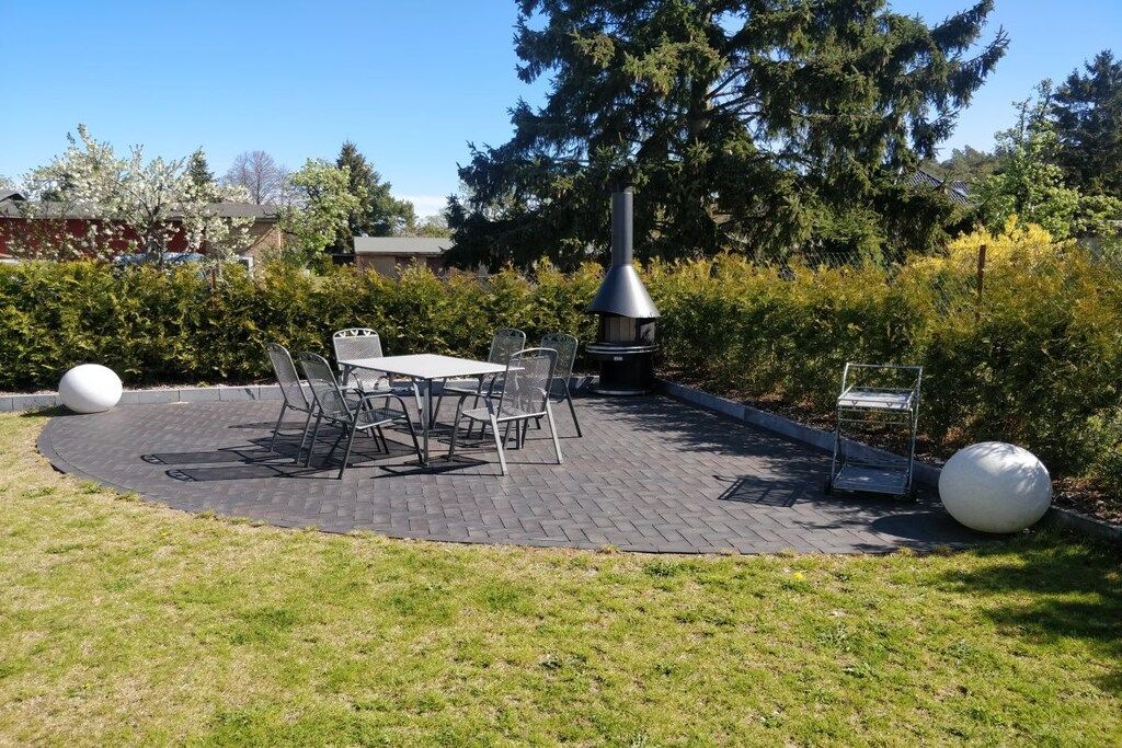 An outdoor patio with a table and chairs, surrounded by hedges and trees.