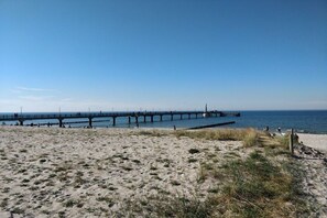 A beach with a pier extending into the water, sandy beach, and clear sky. - Holiday home with 1 bedroom (Fuhlendorf)