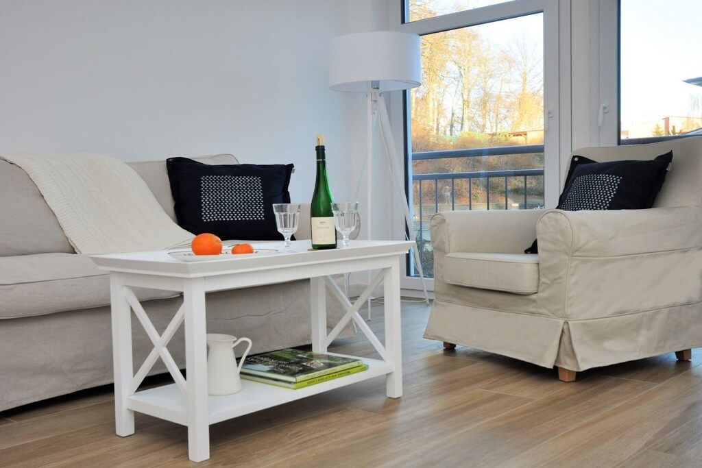 A modern living room with a white sofa, a white coffee table, a lamp, and a view of trees through a window.