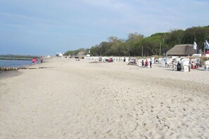 Une plage de sable où se trouvent quelques personnes et quelques constructions, dont un bâtiment surmonté d’un toit de chaume.