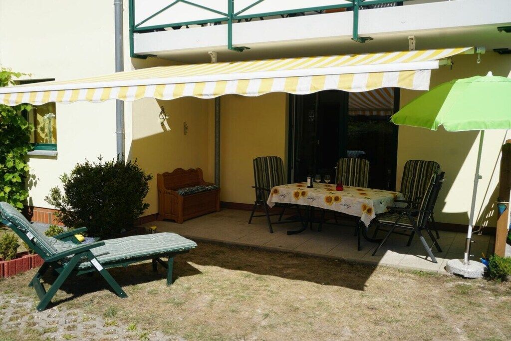 Um pátio com mesa, cadeiras, uma poltrona e um toldo listrado.