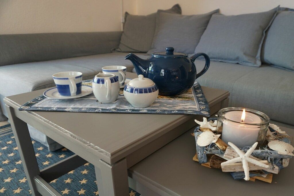 A cozy seating area with a table set for tea, a blue teapot, and a candle surrounded by seashells and starfish.