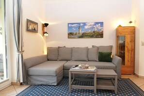 A living room with a grey sofa, a small table, a blue star-patterned rug, a wooden cabinet, and a painting of a lighthouse. - Holiday apartment with 2 bedrooms (Kühlungsborn)