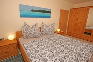 Ein Schlafzimmer mit einem Bett, zwei Nachttischen, einem Holzschrank und einem Bild mit einer Strandansicht.