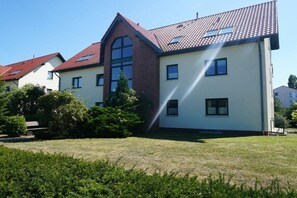 Ein Wohngebäude mit rotem Ziegeldach, zahlreichen Fenstern und einem gepflegten Rasen.