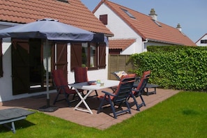 A patio with a table and chairs, a covered umbrella, and a hedge in a residential setting. - Holiday home in de Haan with swimming pool (de Haan)