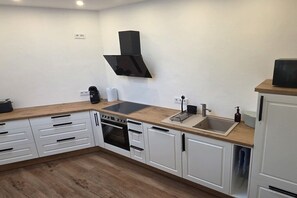 Eine moderne Küche mit weißen Schränken, einer Holz Arbeitsplatte, einem eingebauten Backofen, einer Spüle und einer schwarzen Dunstabzugshaube.
