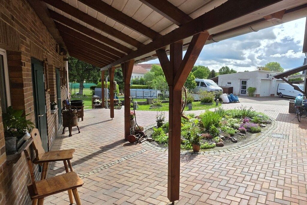 A covered outdoor area with brick flooring, wooden benches, and potted plants.
