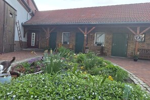 Ein Backsteinhaus mit einem Ziegeldach, ein Garten mit verschiedenen Pflanzen und eine Katze im Vordergrund.