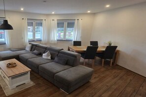 Una sala de estar moderna con un sofá seccional gris, una mesa de centro de madera y un comedor con mesa y sillas de madera.