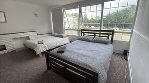 A bedroom with two single beds, a white fireplace, and large windows with a view of a parking lot. - Charming 6-bedroom house in serene Erith perfect for families (Erith)