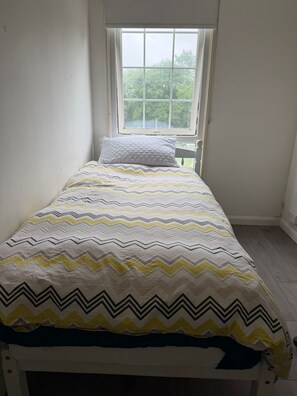 Cama de solteiro com colcha estampada num quarto de paredes brancas e janela.