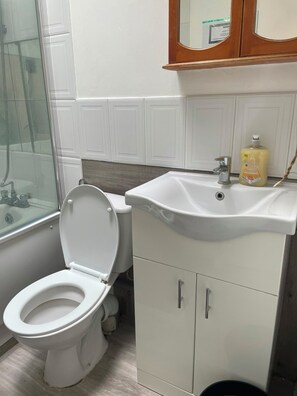 A bathroom with a toilet, a sink, and a mirror above it. - Charming 6-bedroom house in serene Erith perfect for families (Erith)