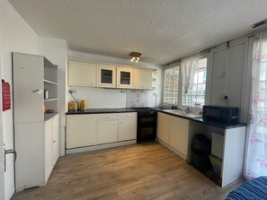 A compact kitchen with white cabinets, a black stove, a microwave, and a sink. - Charming 6-bedroom house in serene Erith perfect for families (Erith)