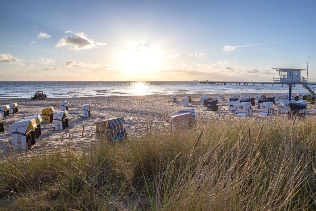 A beach with beach huts, a lifeguard tower, and a pier in the background.