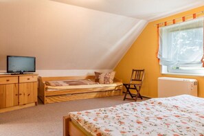A room with a bed, a wooden cabinet, a television, a window with curtains, and a radiator. - Holiday home in Bannemin with swimming pool (Bannemin)