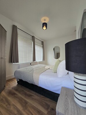 A bedroom with a bed, curtains, a bedside lamp, and a mirror. - Modern Apartment w/ Free Parking & Fast WiFi (Gloucestershire)