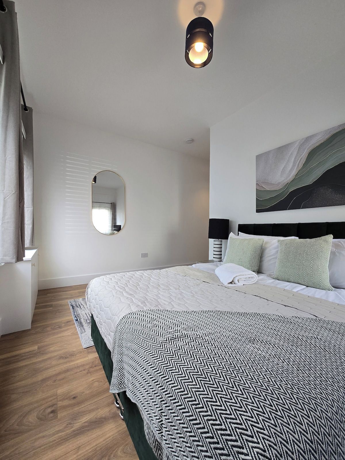 Une chambre à coucher avec un grand lit, une table de chevet, un miroir et une œuvre d’art accrochée au mur.