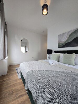 Een slaapkamer met een groot bed, een nachtkastje, een spiegel en een kunstwerk aan de muur.