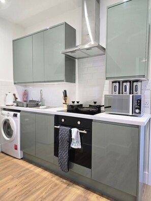A modern kitchen with grey cabinets, a stainless steel range hood, a built-in washing machine, and a microwave. - Modern Apartment w/ Free Parking & Fast WiFi (Gloucestershire)