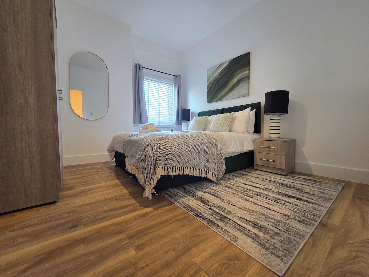 Une chambre à coucher avec un lit, des tables de chevet, un miroir et une fenêtre avec des rideaux.