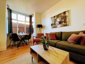 A living room with a sofa, a coffee table, a dining table with chairs, and a window with curtains. - Modern Apartment w/ Free Parking & Fast WiFi (Gloucestershire)